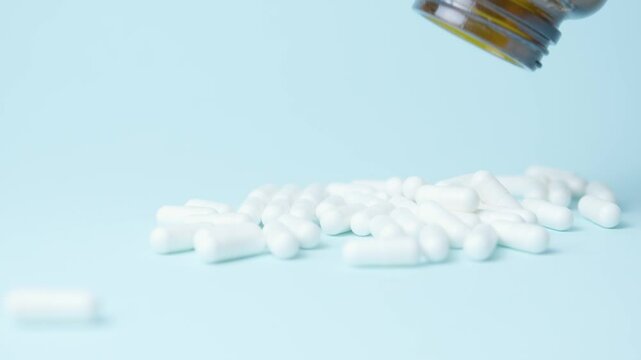 Jar with bunch of white capsules pills poured on blue background. Close up. High quality 4k footage