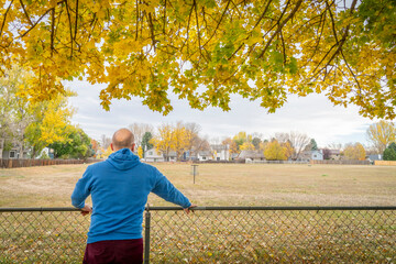 senior man contemplating fall landscape under maple tree in his backyard