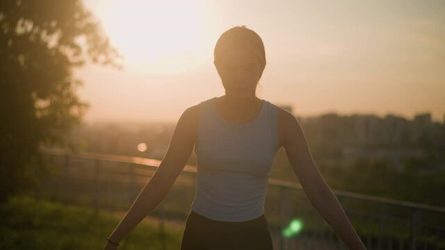 White lady roller skating outdoors under warm sunset glow, silhouetted against vibrant sunlight, with iron railing blurred behind her and distant cityscape