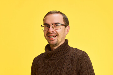 Obraz premium Portrait of young attractive man dressed brown sweater looking at camera with cheerful smile against yellow studio background. Concept of human emotions, beauty and fashion,