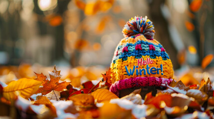 Colorful knitted winter hat with Hello Winter text on autumn leaves background