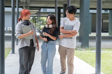 Three young and diverse college students are walking together on a modern university campus, carrying laptops and notebooks and engaging in lively conversation