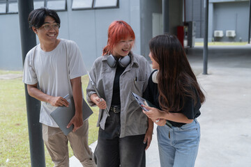 Three young students are happily walking and talking together on campus, carrying laptops and...