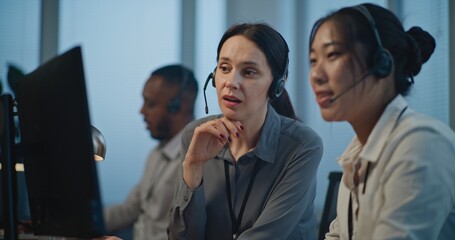 Modern call center office: Two female hotline operators in headsets use computer while...