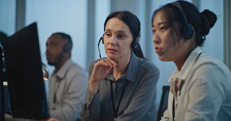 Modern call center office: Two female hotline operators in headsets use computer while...