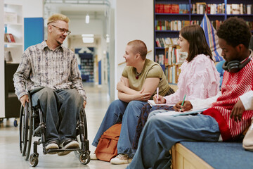 Group of diverse students conversing in library setting including individual in wheelchair engaging with peers surrounded by books and comfortable seating areas