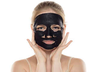 Beautiful young smiling woman posing with a facial black paper mask on her face. Skin care and treatment, spa, natural beauty and cosmetology concept.