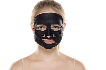Beautiful young woman posing with a facial black paper mask on her face. Skin care and treatment, spa, natural beauty and cosmetology concept.