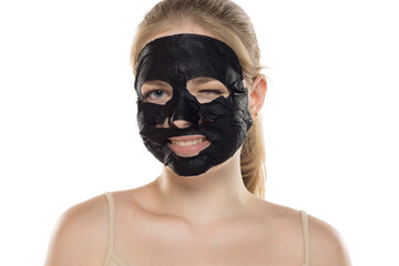 Beautiful young smiling woman posing with a facial black paper mask on her face. Skin care and treatment, spa, natural beauty and cosmetology concept