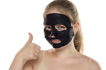 Beautiful young happy woman posing with a facial black paper mask on her face. Skin care and treatment, spa, natural beauty and cosmetology concept