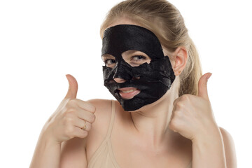 Beautiful young happy woman posing with a facial black paper mask on her face. Skin care and treatment, spa, natural beauty and cosmetology concept