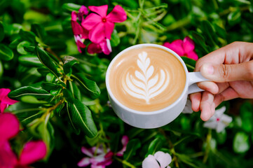 A woman's hand is holding a latte coffee cup.Using skills in making latte menus.Drink coffee in the...