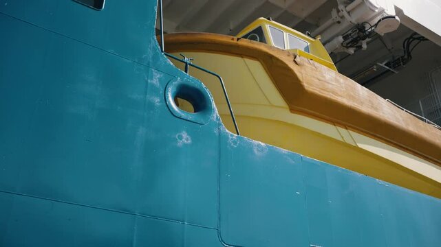 Yellow rescue boat hanging on the side of a large turquoise ship. The boat is secured to the hull and ready for use in case of emergency