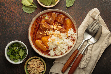 Steaming bowl of massaman curry with beef, potatoes, and coconut milk sauce, served with rice and peanuts, a traditional flavorful thai meal