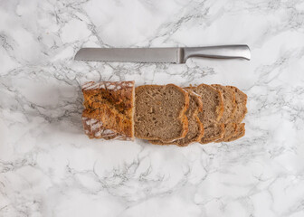 Sliced loaf of bread with a silver knife on the side. Flat lay of cut bread on a marble counter. 