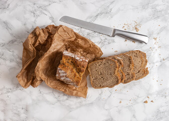 Sliced loaf of bread with a silver knife on the side. Flat lay of cut bread on a marble counter. 
