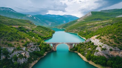 The lake water is blue-green, surrounded by green mountains and forests on both sides of the river, with an ancient stone arch bridge across it
