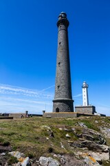 Ile Vierge Lighthouse stands tall against a backdrop of another old lighthouse and a clear blue sky