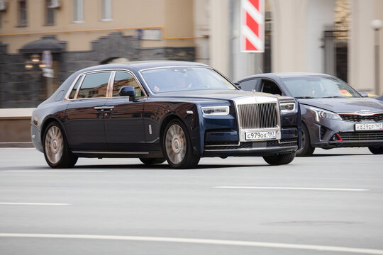 Front side view rolling shot of blue color sedan car in motion. Rolls-Royce Phantom driving along the street in city with blurred background