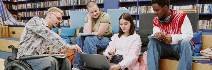 Group of diverse students collaborating and sharing ideas in a modern library study area. Various resources are present, including laptops, notebooks, and books
