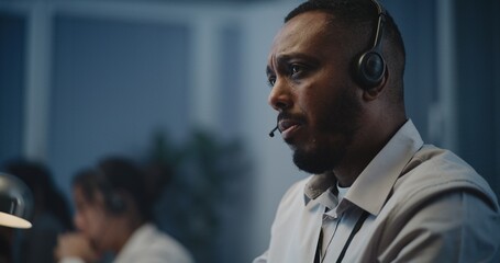 Modern call center office of mental health line: Close up portrait of African American hotline specialist in headset sitting at computer, listening person, providing online psychological assistance.