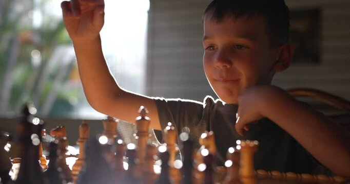 Young boy playing chess against himself leans over board to play opposite pieces