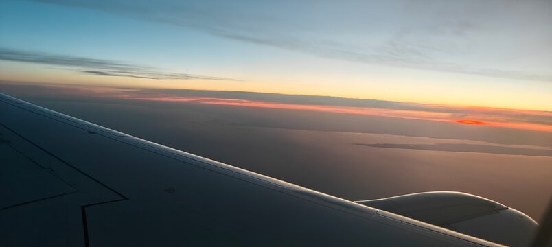 An airplane wing during flight with a beautiful sunset horizon in the background, blending colors of orange and blue