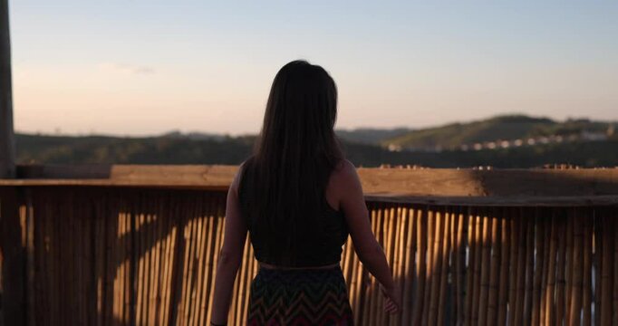 Young woman walks to look out over fense into rolling hills of grapes and coffee beans - South America