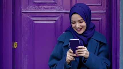 Smiling Hijab-Wearing Woman with Smartphone in Front of Purple Wall