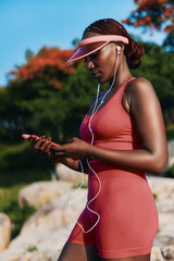 Young woman wearing workout attire, listening to music outdoors with headphones