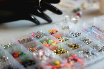 Hand figurine, colorful friendship bracelets, necklaces, various beads and DIY supplies on the table. Making jewelry at home. Selective focus.