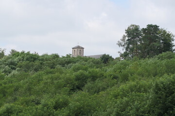 A tall church tower peeks out from behind a cluster of lush green trees.