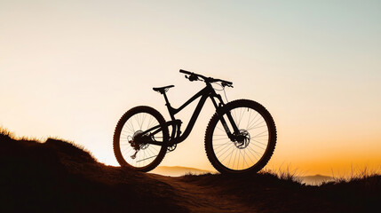 Obraz premium Silhouette of a mountain bike on a hilltop during a sunset with an orange and pink gradient sky.