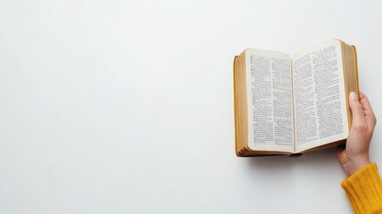 Obraz premium A woman's hand gracefully holds an open book under soft light, capturing the essence of reading against a serene white backdrop