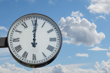 street clock showing twelve hours and one minute against a cloudy blue sky