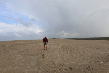 Obraz premium lone walker crosses the sandy dunes of the desert carrying a backpack on shoulders