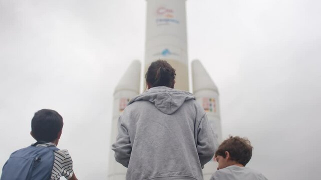 Family marvels at a giant rocket. Space exploration, wonder, inspiration, cloudy sky, childhood dreams.