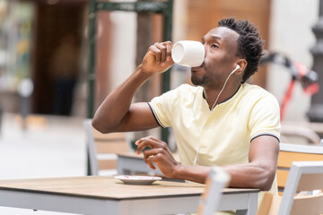 Man using smartphone voice feature, smiling, holding coffee cup, seated in outdoor cafe