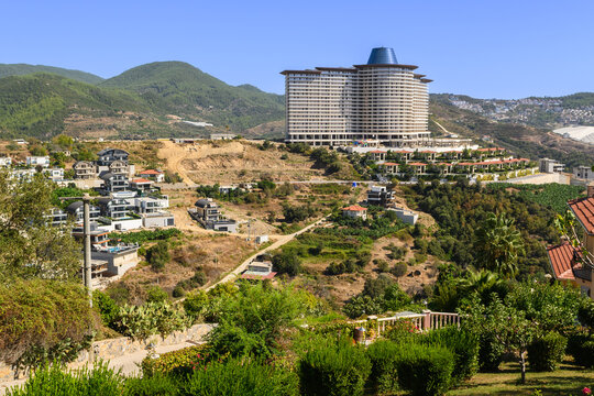 A panoramic view of a developing hillside community near a modern hotel under a clear blue sky
