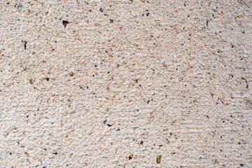  Close-up of a textured surface, likely concrete or a wall, with specks of black, brown, and red. The overall color is light beige or off-white.
