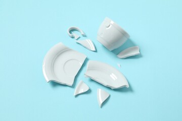 White cup and plate broken on color background