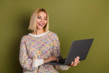 Smiling woman in colorful sweater using laptop against khaki background, expressing joy and engagement in technology