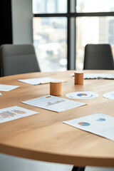 Naklejka premium Round conference table in meeting room with business documents, chairs, and window view of cityscape in the background.