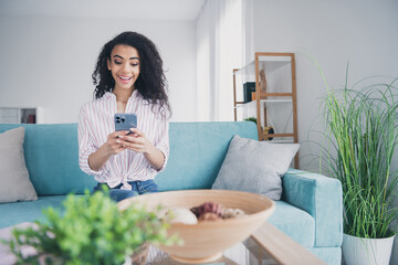 Portrait of nice young woman use phone sit sofa wear striped shirt pastime modern interior flat...