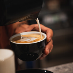 A barista pours steamed milk into a cup of coffee, creating latte art. Close up.