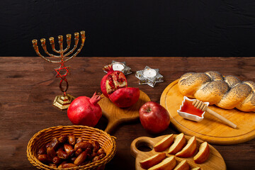 Challah, honey, apple and pomegranate and burning candles on wooden table with menorah Rosh...