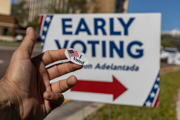 Hand holding a sticker that says I Voted, on early vote poster background. Conceptual photo