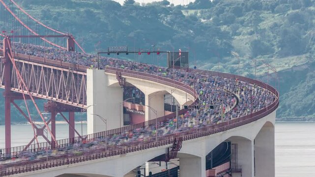 Running Lisbon half marathon crossing the 25 of April bridge over the Tagus river aerial timelapse view from above. Big crowd moving down the bridge from start to finish. Close up to curved road