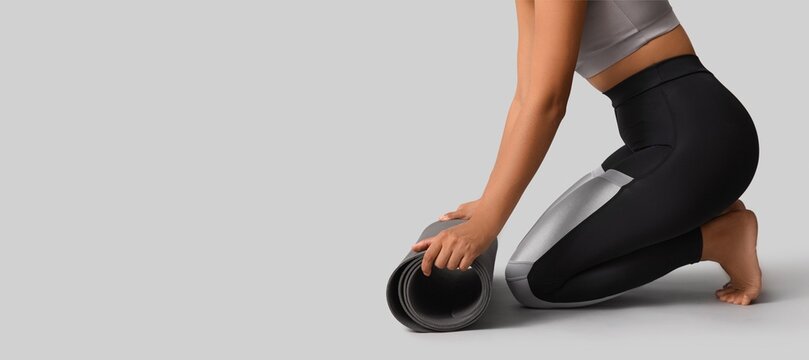 Sporty young African-American woman rolling out yoga mat on grey background with space for text