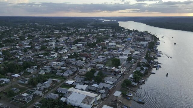 Drone orbits from high over city to over river at sunset in Oiapoque, Amap&aacute;, Brazil